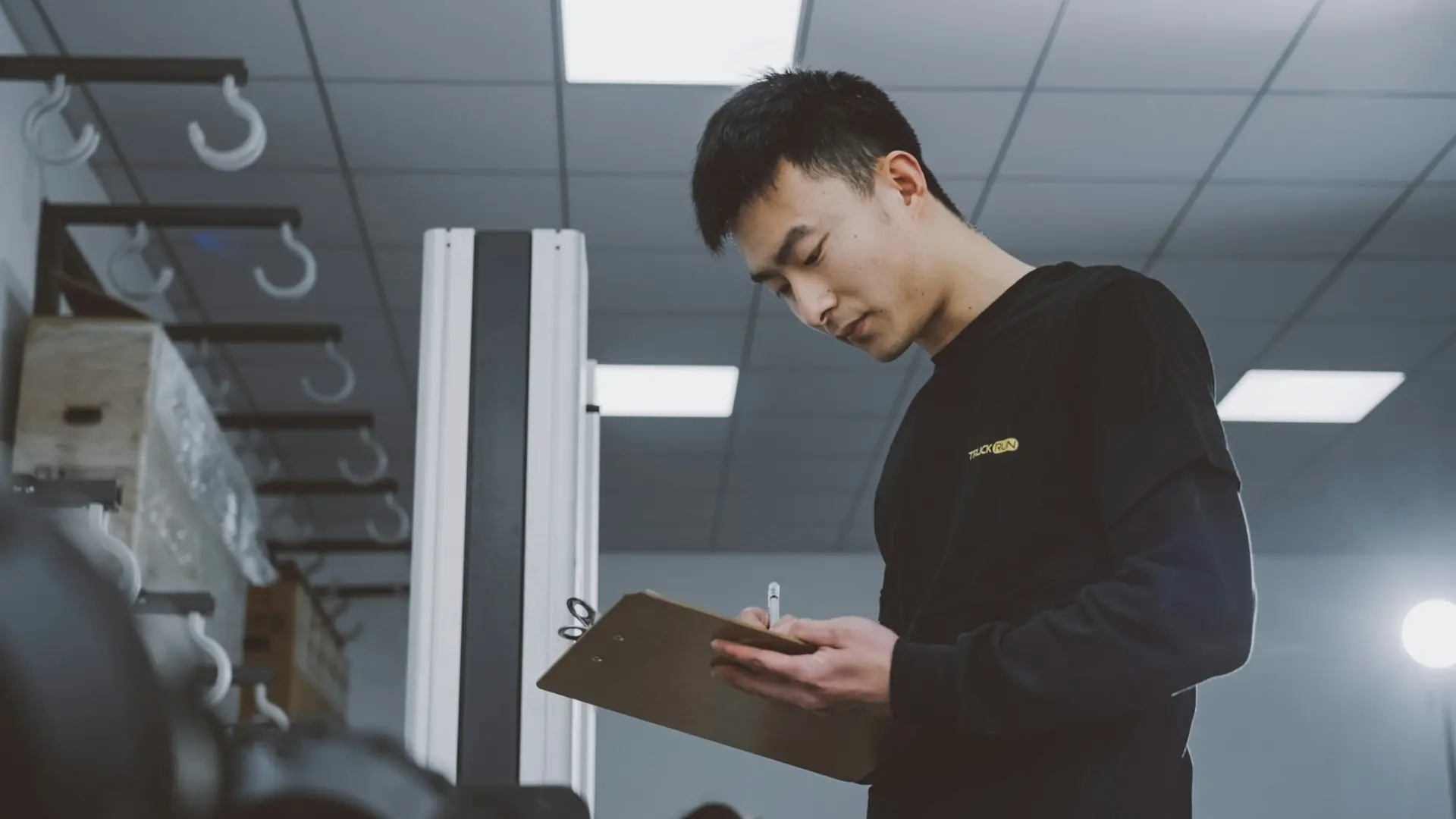 A man reading papers on a clipboard in a bright, tidy workshop