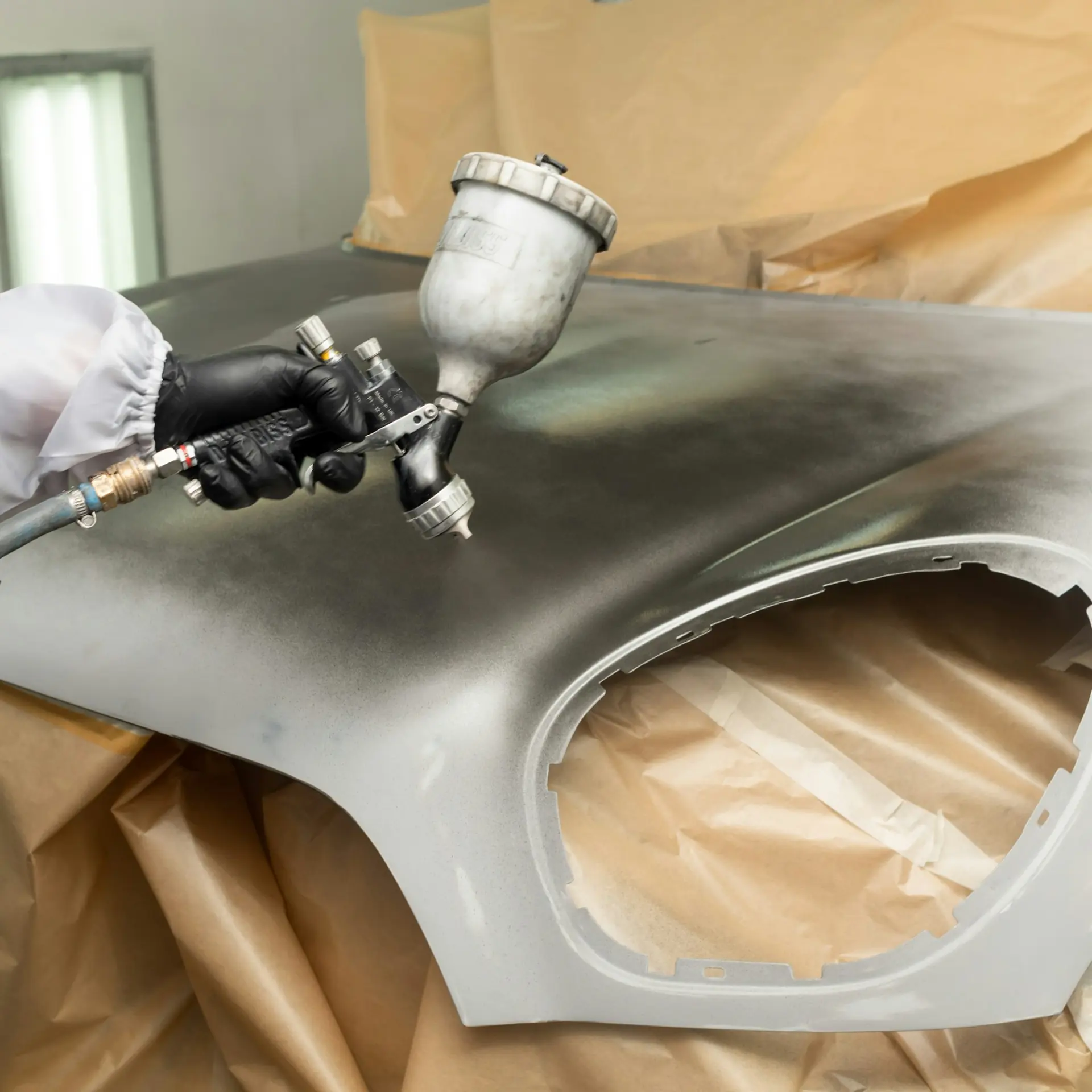 A gloved hand spraying silver paint onto a loose front wing laid on masking paper