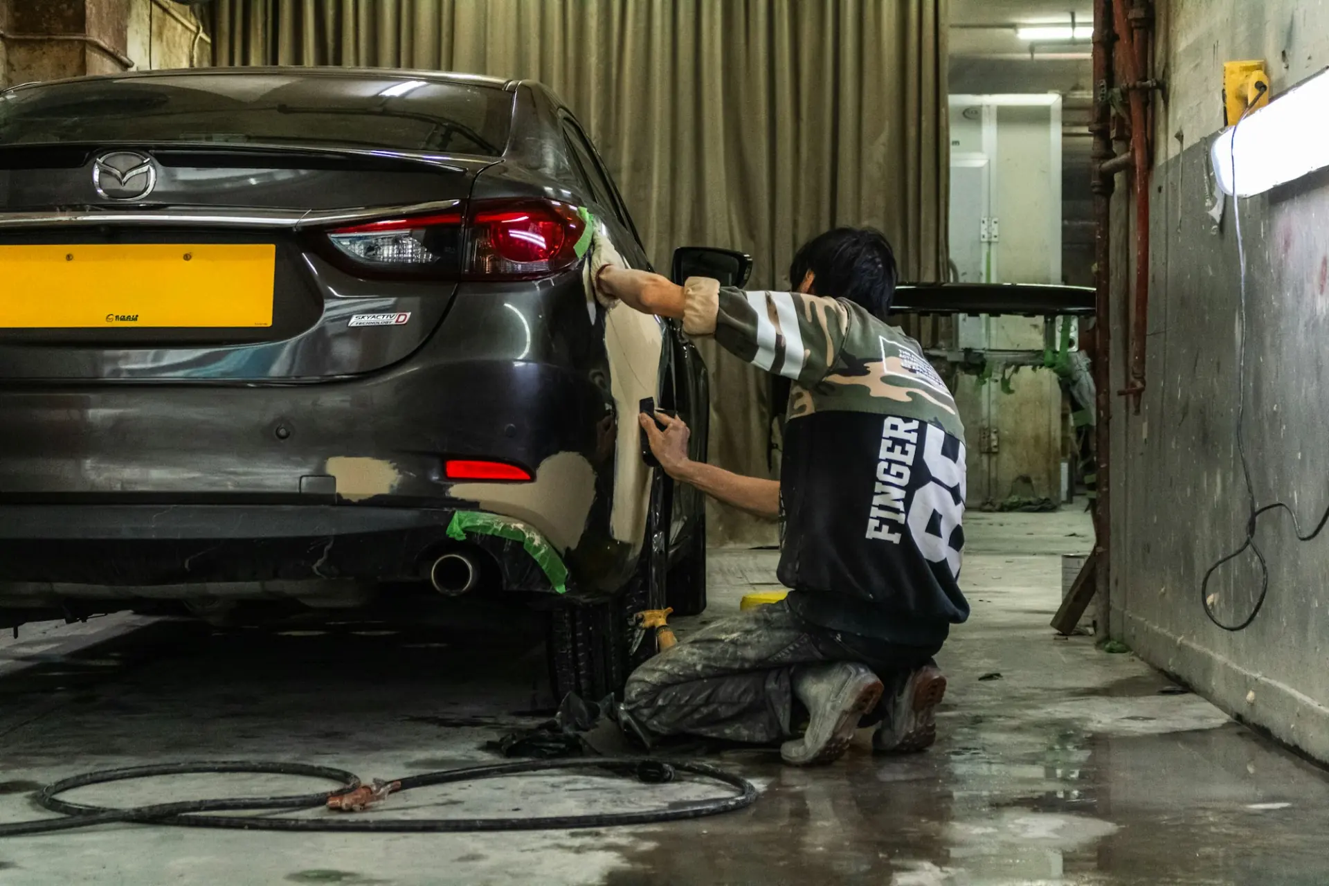 A technician sanding the rear panel of a grey car in a workshop before painting