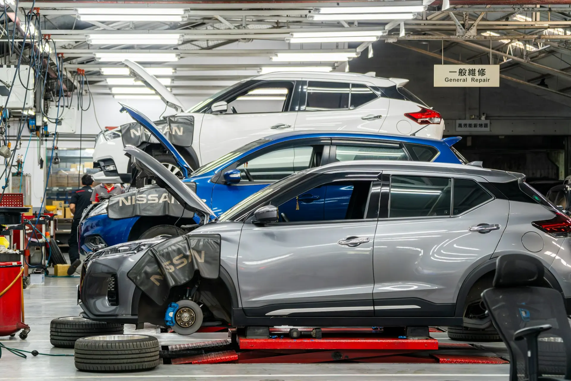 Cars on stands in a body shop, one with its front wheel and bumper off for repair