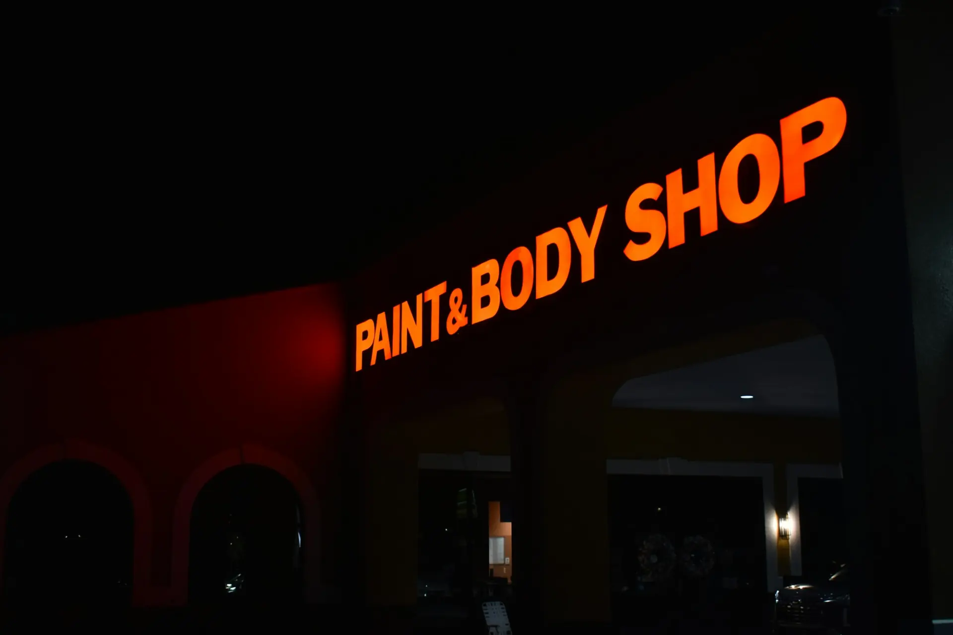 An illuminated Paint & Body Shop sign on a workshop building at night