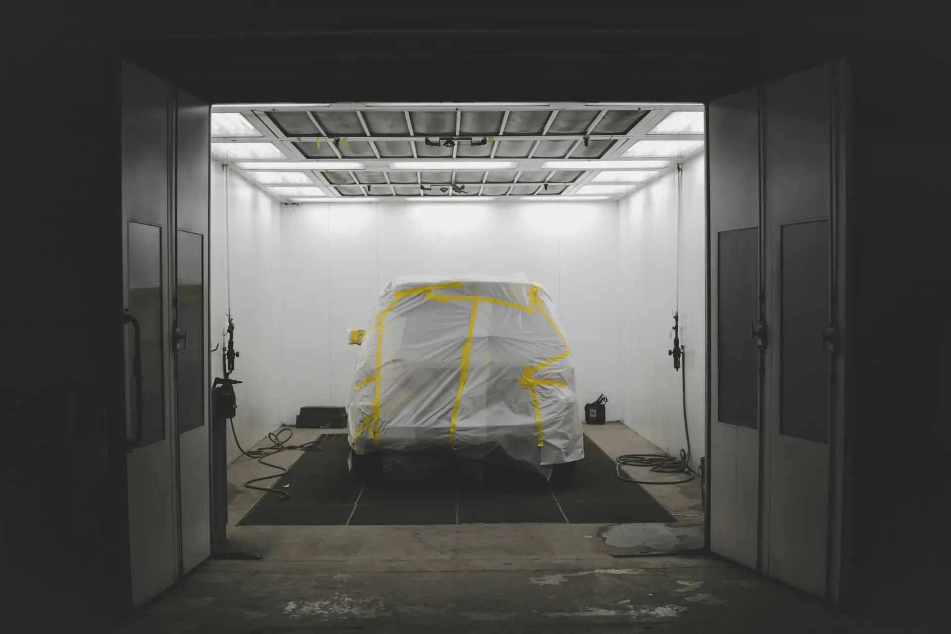 A car masked in plastic waiting inside a lit spray booth