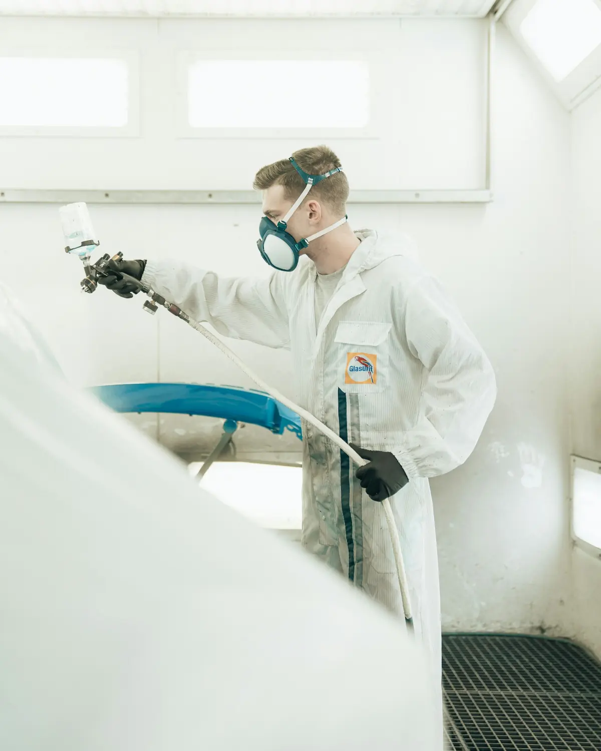 A spray painter in a protective suit, gloves and respirator painting a panel in a spray booth