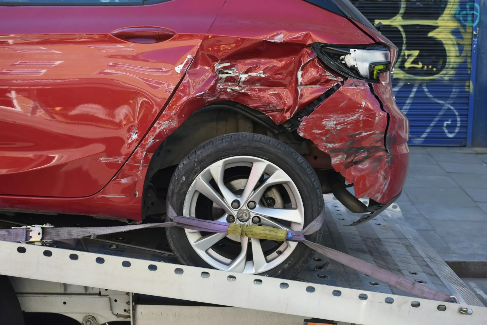 A red car with accident damage loaded on the back of a flatbed tow truck